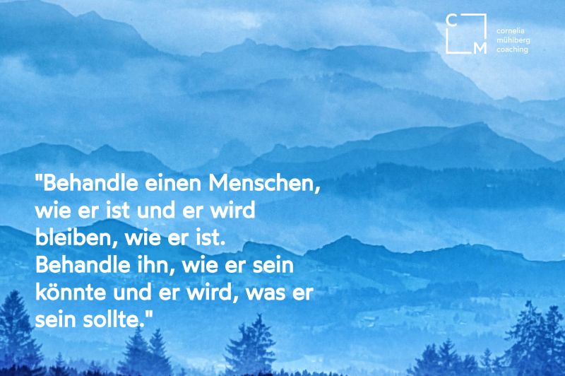 Im Hintergrund ist eine Berglandschaft in blau zu sehen, der Text besagt "Behandle einen Menschen, wie er ist und er wird bleiben wie er ist. Behandle ihn, wie er sein könnte und er wird, was er sein sollte."