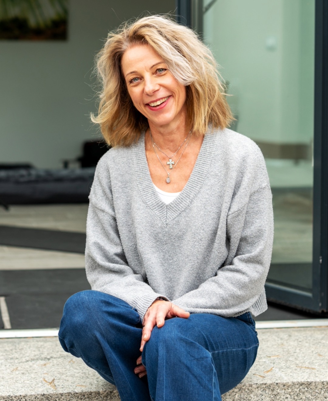 Frau im hellgrauen Pullover sitzend auf einer Treppe vor dem Eingang